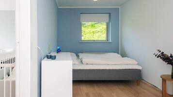 A bedroom with a bed, a bedside table, a window, and a crib.