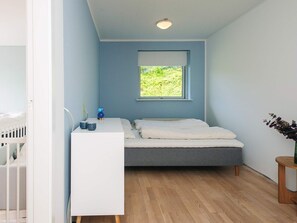 A bedroom with a bed, a bedside table, a window, and a crib.