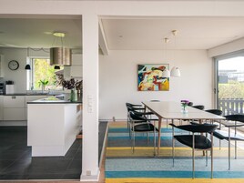 Una cocina moderna con una isla central, un comedor con mesa y sillas, y un ventanal que ofrece vistas al verdor.