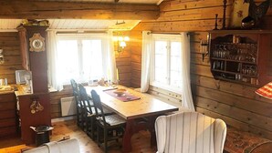 A cozy cabin interior with a wooden dining table, chairs, a cushioned armchair, and a shelf with glassware. - 8 Person Holiday Home in Etnedal-by Traum (Etnedal)