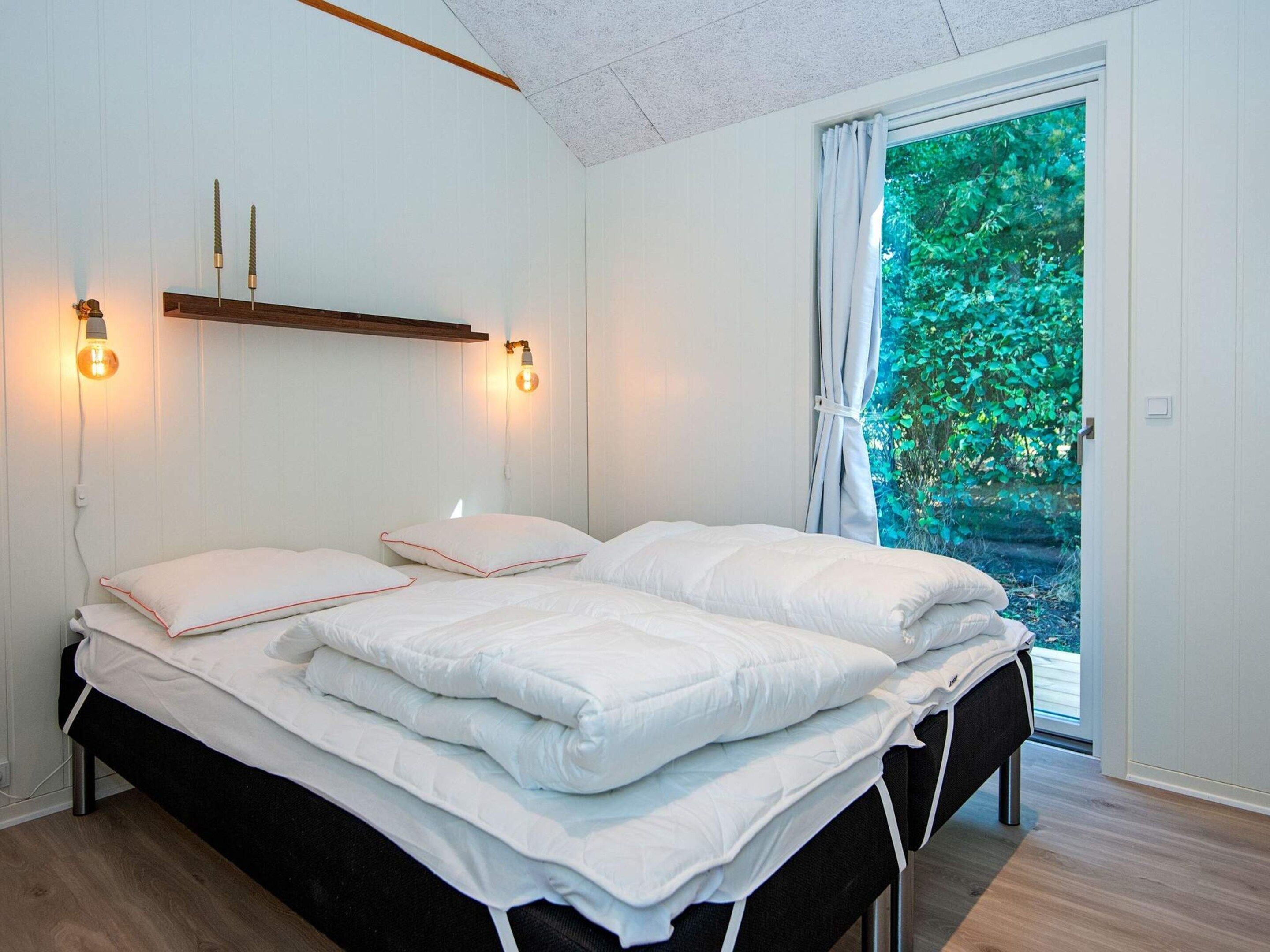 A bedroom with a bed, bedside lamps, and a view of greenery outside.