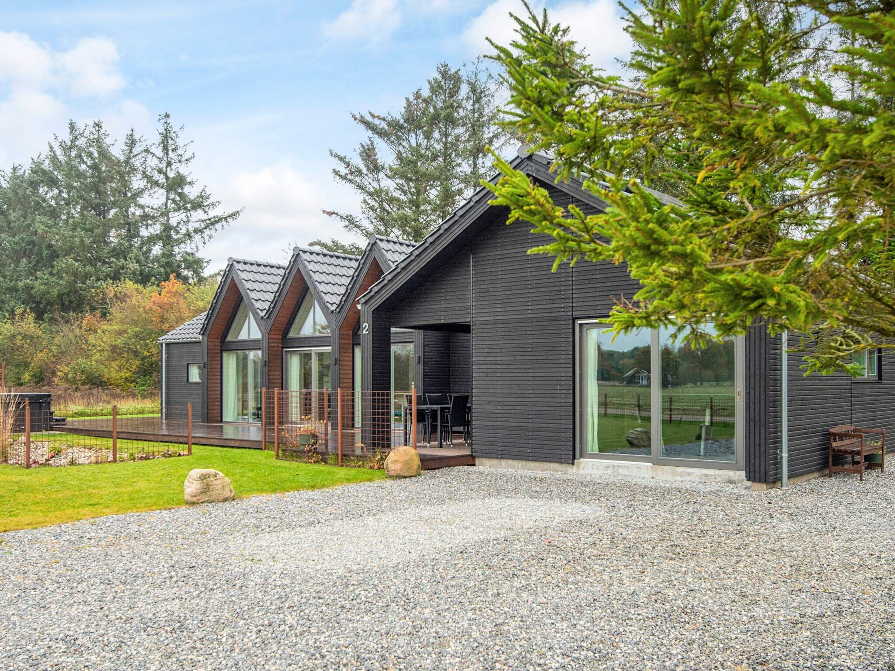Eine moderne Hütte mit Kiesweg, großen Fenstern und einer Holzterrasse.