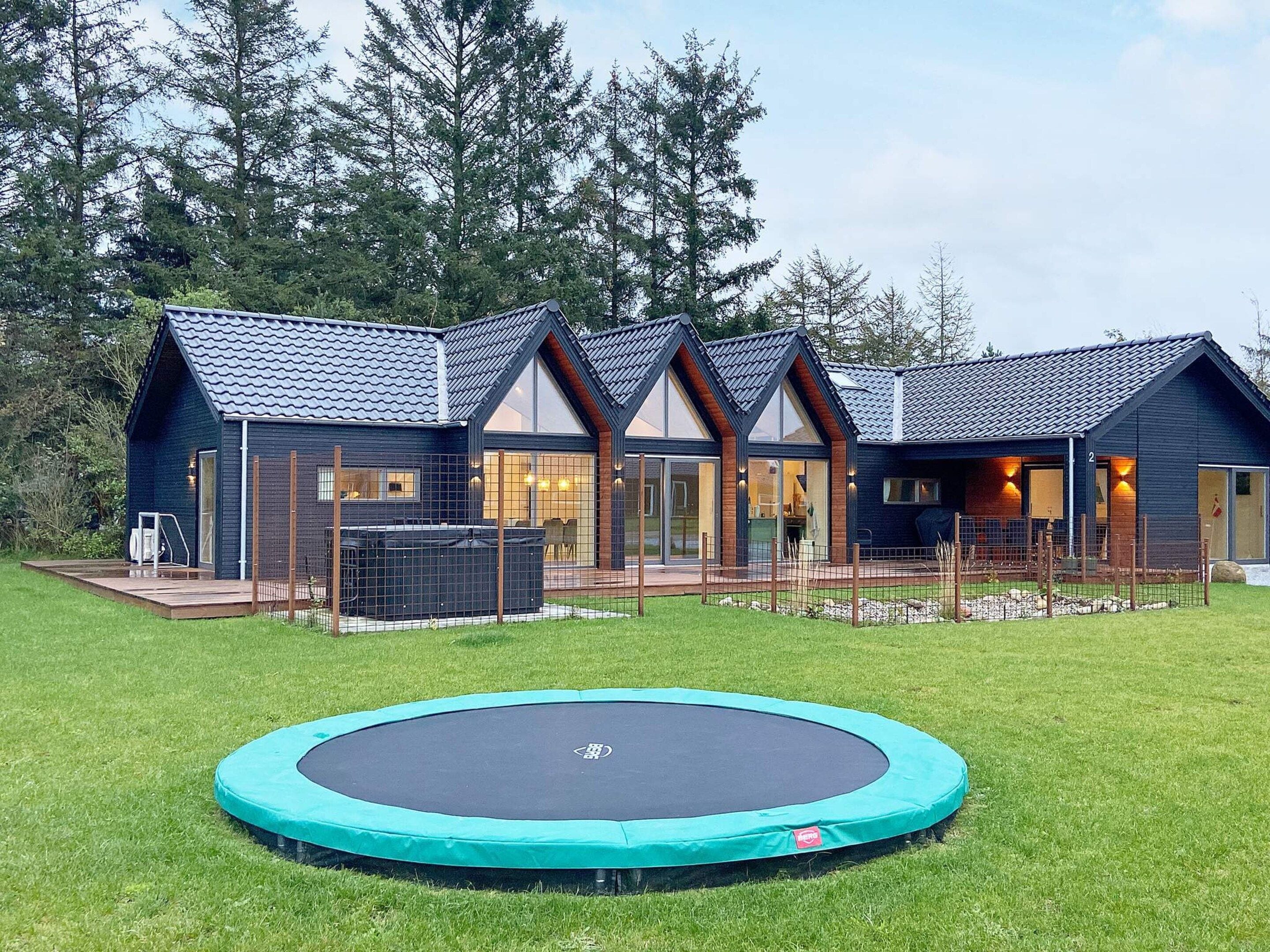 Ein modernes Haus mit einem großen Garten, einem Trampolin und einem eingezäunten Bereich.