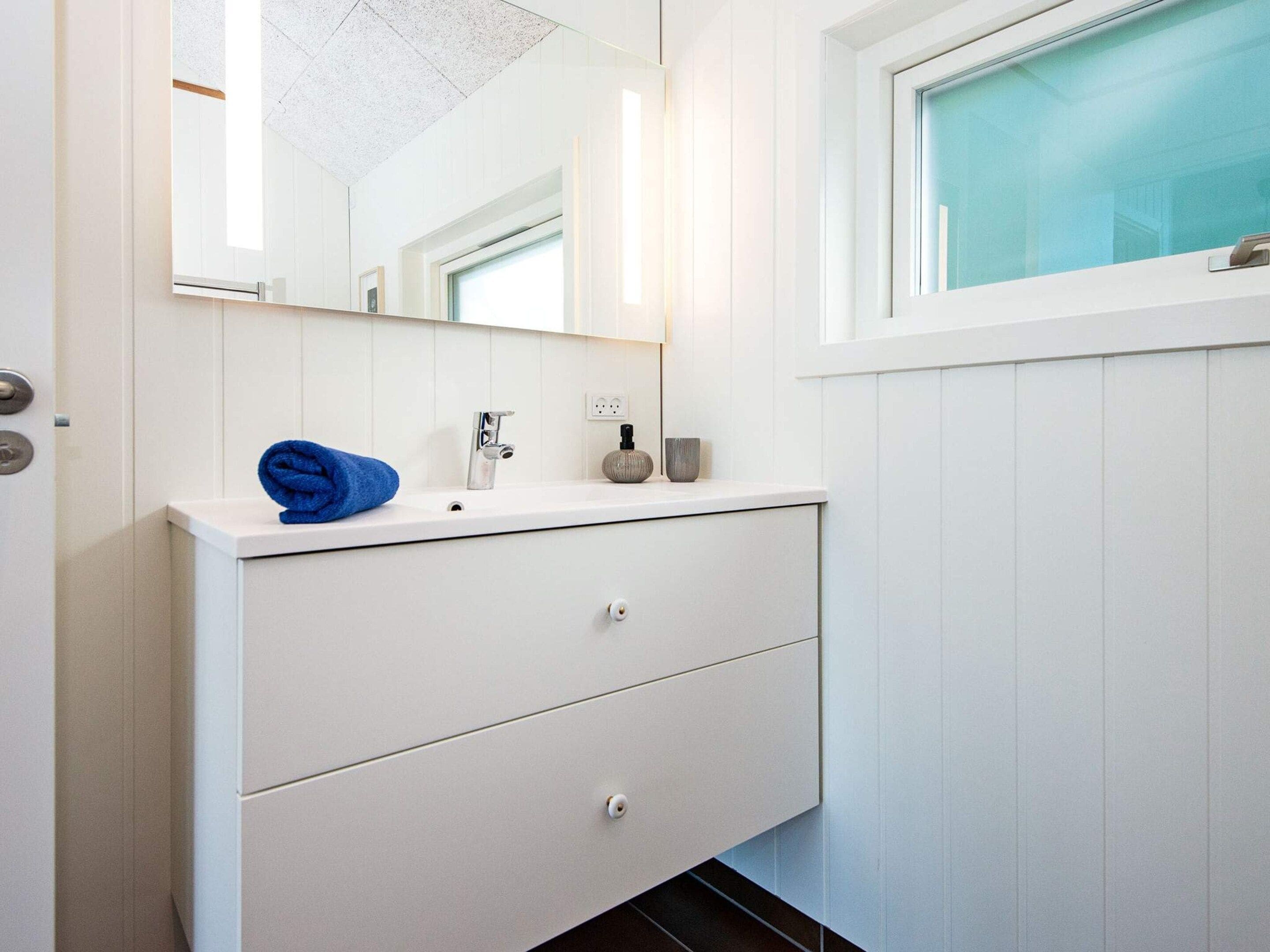 A bathroom with a white vanity, a mirror, a towel, and a window with a view.