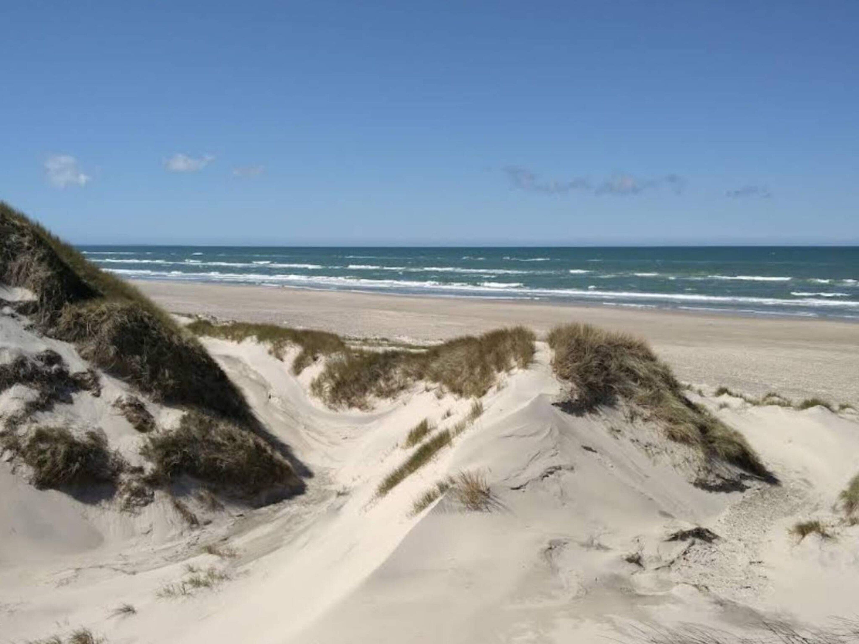 A beach with sand dunes and ocean waves.
