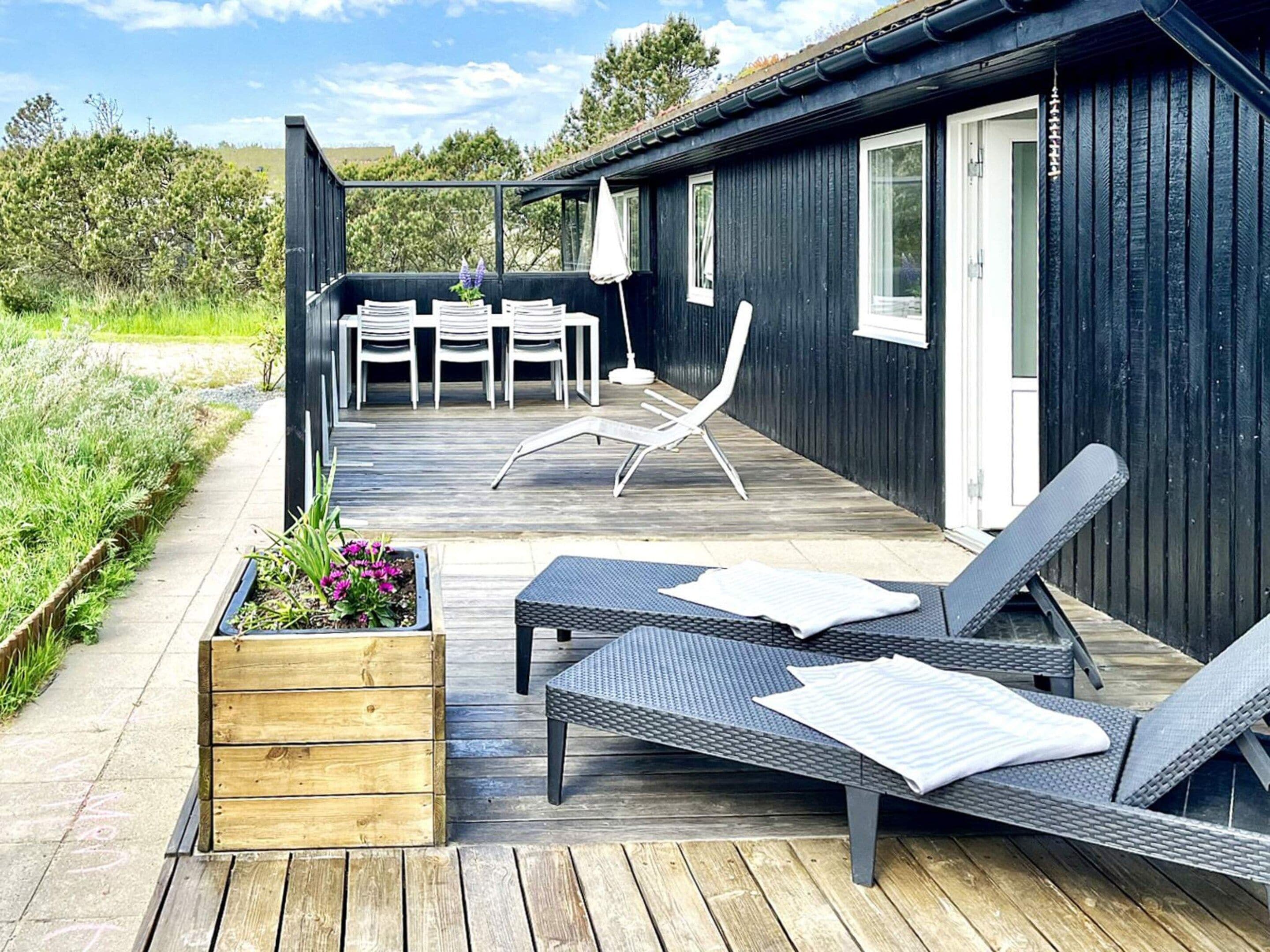 A deck with outdoor furniture, a wooden planter with flowers, and a building with a dark exterior.