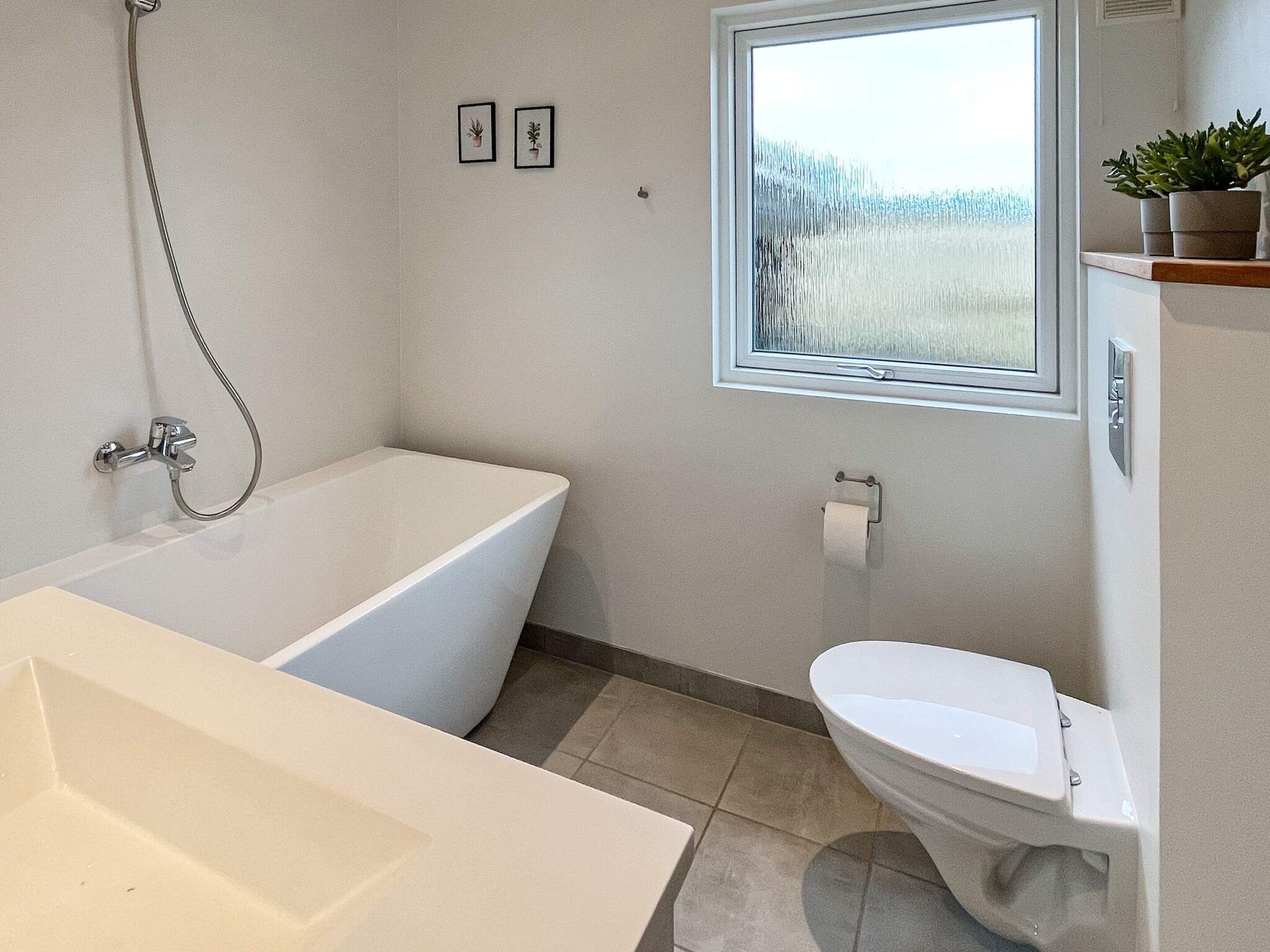 A bathroom with a bathtub, toilet, and a window with a view.