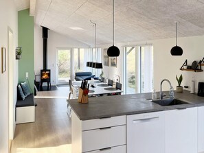A modern kitchen with a central island, a dining area with a sofa, and a view of the outdoors. - 6 Person Holiday Home in Saltum (Saltum)