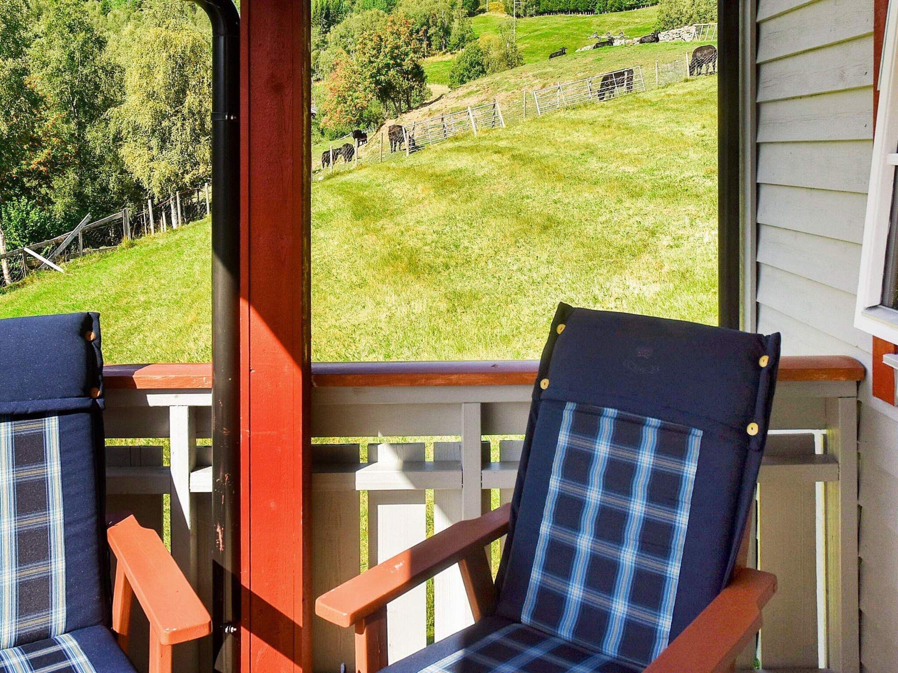 A porch with two plaid chairs and a view of a grassy field with cows.