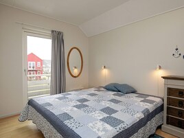 Un dormitorio con una cama grande, una ventana con cortinas, un espejo montado en la pared y un aparador con cajones.