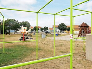 Een speeltuin met groene metalen frames, een picknicktafel en een speeltoestel.