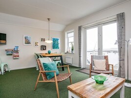 Una habitación con una mesa de comedor, sillas, un tazón verde, una lámpara colgante y vistas a través de un ventanal grande.