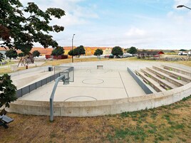 Una cancha de baloncesto con aro, una zona de estar de hormigón y un parque infantil.