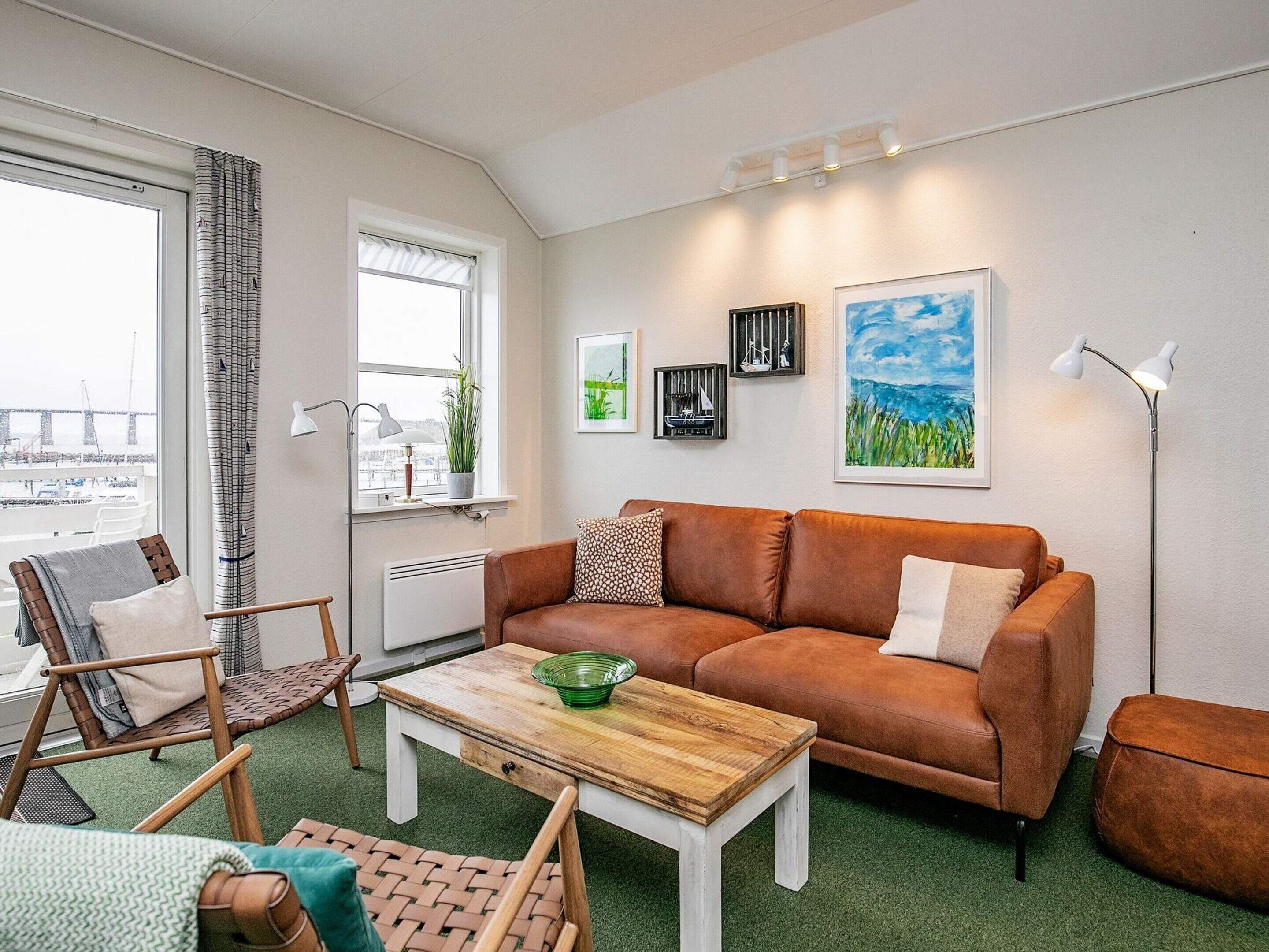 Ein Wohnzimmer mit einem braunen Ledersofa, einem Holztisch und Blick auf eine Stadtansicht durch das Fenster.