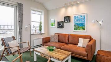 Ein Wohnzimmer mit einem braunen Ledersofa, einem Holztisch und Blick auf eine Stadtansicht durch das Fenster.