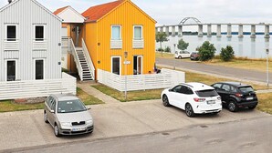 A two-story building with a red roof and a white facade, adjacent to a white building with a grey roof. There are three cars parked in front, and a bridge is visible in the background.