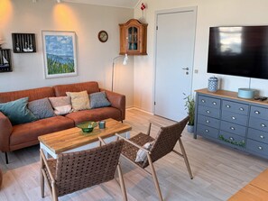 A living room with a brown leather sofa, a wooden coffee table, wicker chairs, a television on a cabinet, and a painting on the wall. - 4 Person Holiday Home in Rudkobing (Rudkobing)