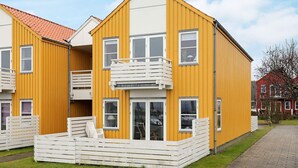 Un bâtiment jaune à deux étages, doté d’un balcon et d’un petit espace extérieur aménagé pour s’asseoir.