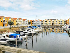 A marina with boats docked, a row of colorful houses, and calm water reflecting the scene. - 4 Person Holiday Home in Rudkobing (Rudkobing)