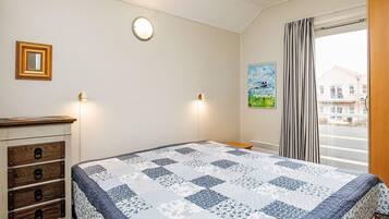 A bedroom with a bed, dresser, wall-mounted lights, a painting, and a view through a window.