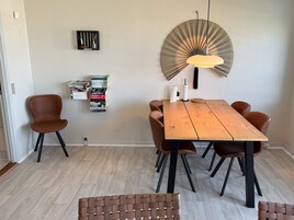 Un comedor con una mesa de madera, cuatro sillas, una lámpara colgante y una estantería de pared.