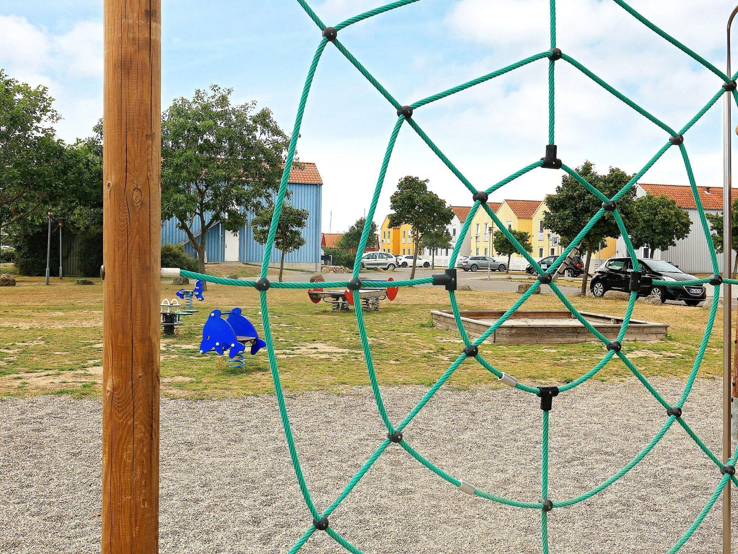 A playground with a rope climbing structure, a wooden post, and a gravel area.