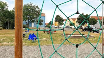 A playground with a rope climbing structure, a wooden post, and a gravel area.