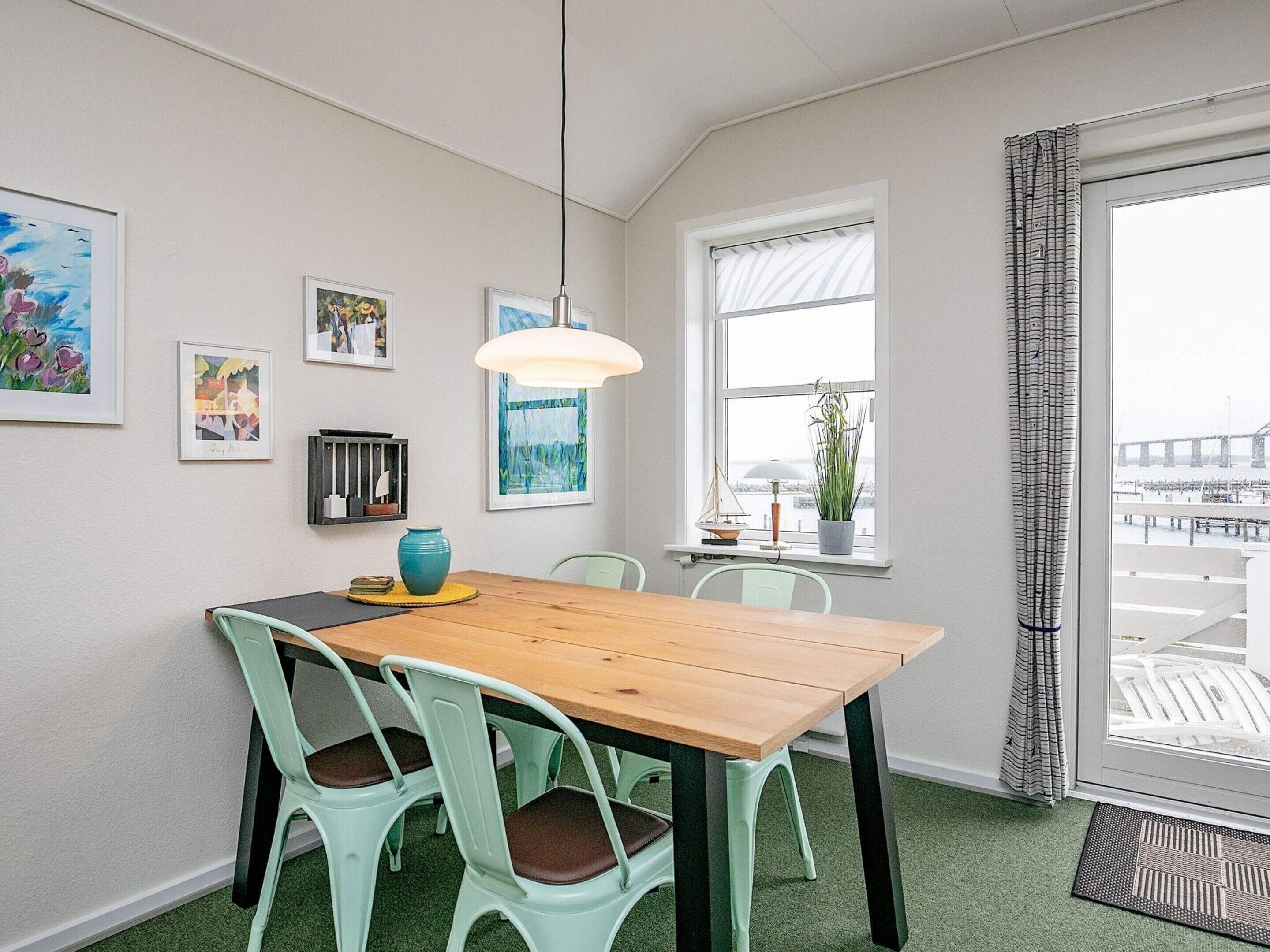 A dining area with a wooden table, green chairs, a hanging light fixture, and artwork on the walls.