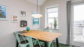 Ein Essbereich mit einem Holztisch, grünen Stühlen, einer hängenden Leuchte und Kunstwerken an den Wänden.