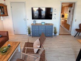 Una sala de estar con televisor, una mesa de centro de madera, un sillón de mimbre marrón y un mueble azul con cajones.