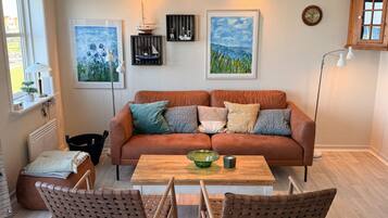 A living room with a brown leather sofa, a wooden coffee table, wicker chairs, and artwork on the walls.
