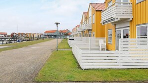 A row of yellow buildings with white balconies, a gravel path, and a grassy area.