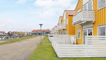 A row of yellow buildings with white balconies, a gravel path, and a grassy area.