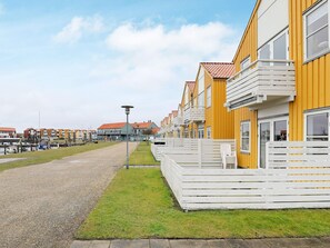 A row of yellow buildings with white balconies, a gravel path, and a grassy area.
