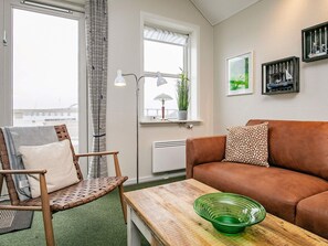 A cozy living room with a brown sofa, a patterned armchair, a wooden coffee table, and a green glass bowl.