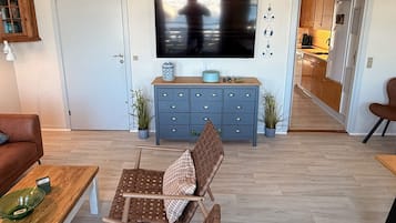 Un soggiorno con televisione, un mobiletto blu, una poltrona in vimini marrone e un tavolino in legno.