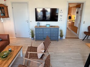 A living room with a television, a blue cabinet, a brown wicker chair, and a wooden coffee table.