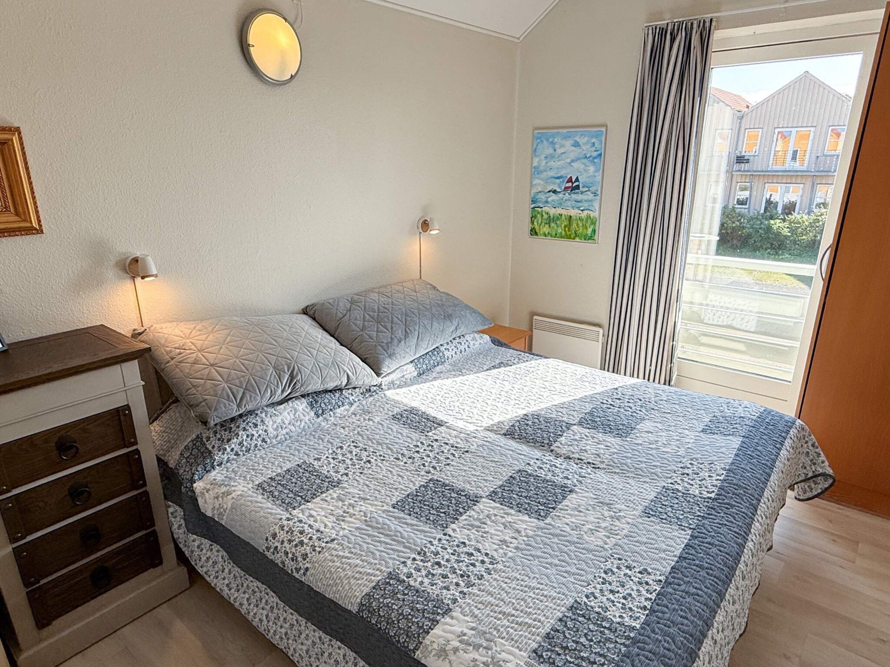 A bedroom with a bed, bedside lamps, a dresser, a radiator, and a window with curtains.