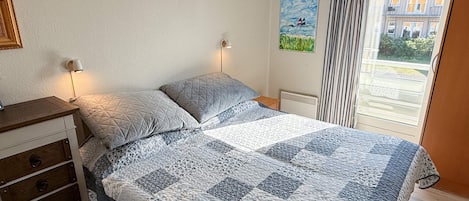 A bedroom with a bed, bedside lamps, a dresser, a radiator, and a window with curtains.
