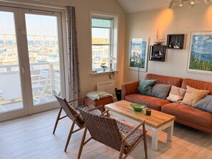 A living room with a sofa, chairs, a coffee table, and a view of a marina through large windows.