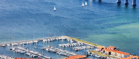 A marina with boats docked, a bridge in the background, and a town with colorful buildings.