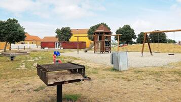 Ein Spielplatz mit Schaukeln, einer Kletterkonstruktion und einem kleinen Gebäude.