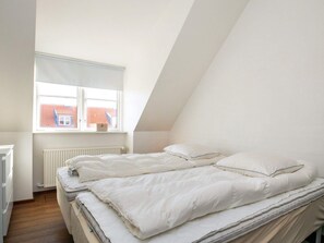 Un dormitorio con techo inclinado, una ventana con vista a un edificio de tejados rojos y un radiador.