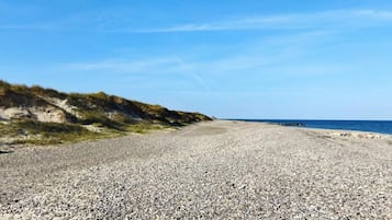 A pebble beach with a clear sky and a distant view of the sea.