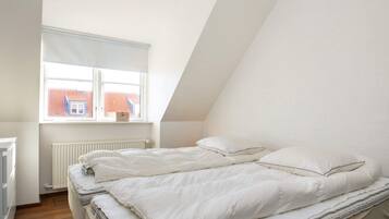 A bedroom with a sloped ceiling, a window with a view of a red-roofed building, a radiator, and a bed with white bedding.