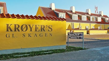 Un edificio amarillo con letrero 'KROYER'S GL. SKAGEN', una señal de calle que indica 'Højensvej 30A-34P' y 'Vandrestien 7-12', y una hilera de edificios similares al fondo.