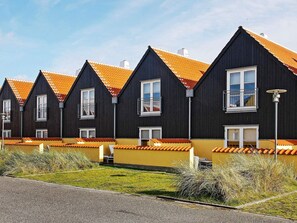 Une rangée de bâtiments aux couleurs sombres, avec des toits recouverts de tuiles orange et des fenêtres à cadre blanc.