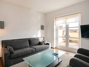 Una sala de estar moderna con un sofá gris, una mesa de centro de vidrio y un televisor montado en la pared.