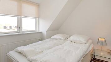 A bedroom with a bed, a window, a radiator, and a bedside table with a lamp.