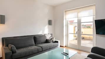 A modern living room with a grey sofa, a glass coffee table, and a television on the wall.